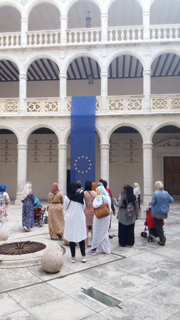 Grupo de mujeres en el patio del Palacio de Santa Cruz, con los arcos de ambos pisos al fondo. Bandera de la UE entre los arcos.
